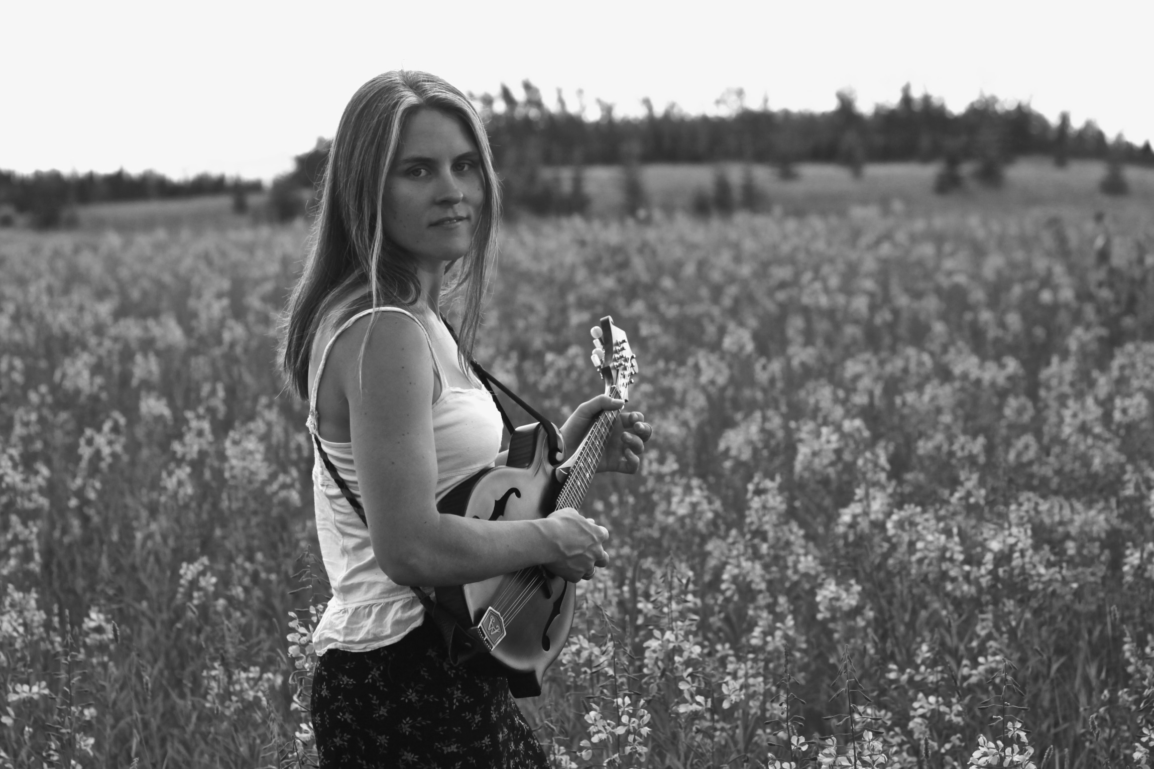 Britt Arnesen standing in a field holding a mandolin.