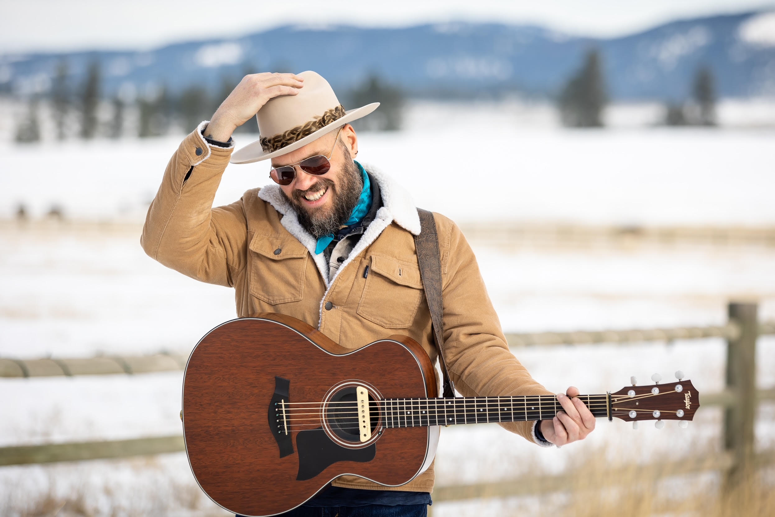 Travis Yost outdoors in the snow, holding an acoustic guitar.