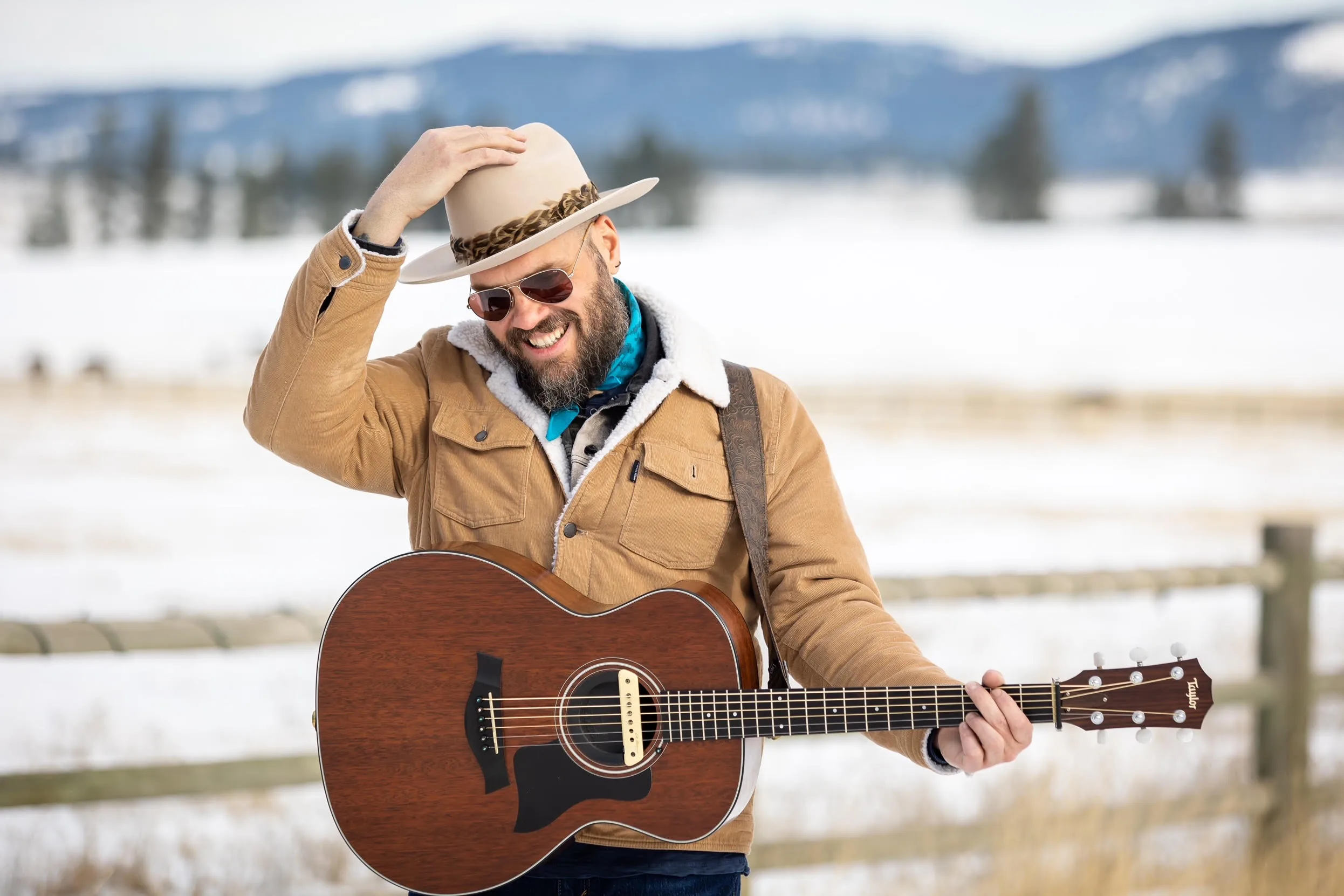 Travis Yost outdoors in the snow, holding an acoustic guitar.
