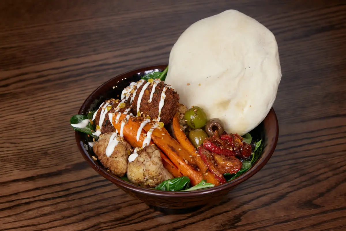 Falafel bowl with pita, roasted carrots, olives, and vegetables.