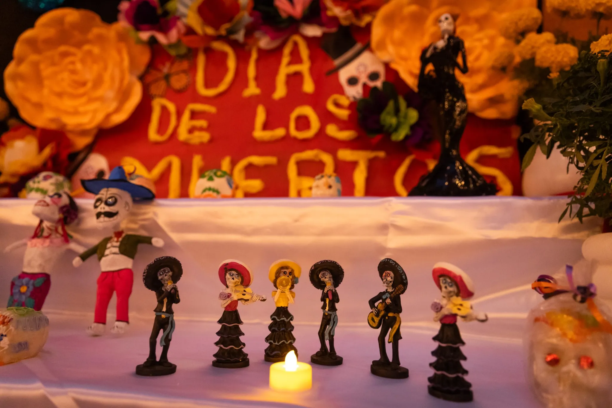 Día de los Muertos altar with colorful skeleton figurines, orange flowers, and a candle.